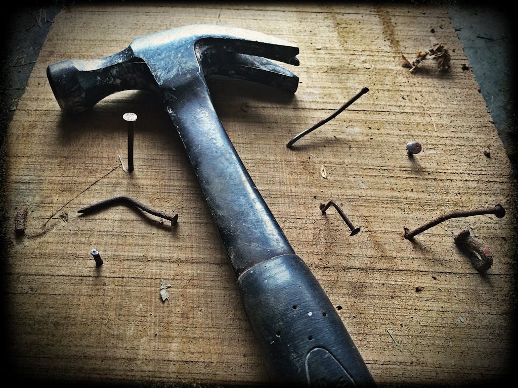 A weathered hammer surrounded by bent nails on a wooden plank, capturing the essence of carpentry work.